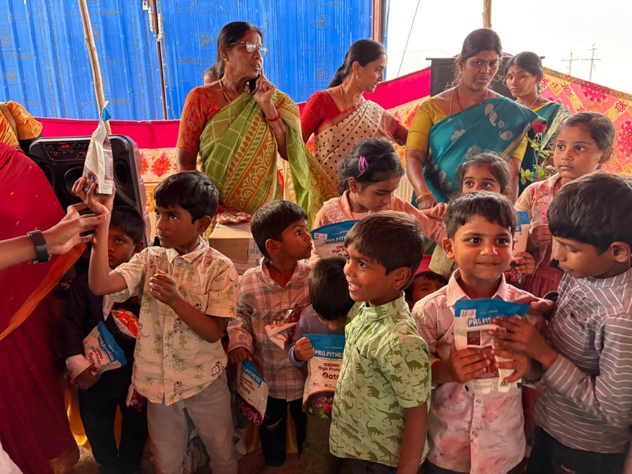 Children queueing with their hands out as volunteers hand out cartons at a camp