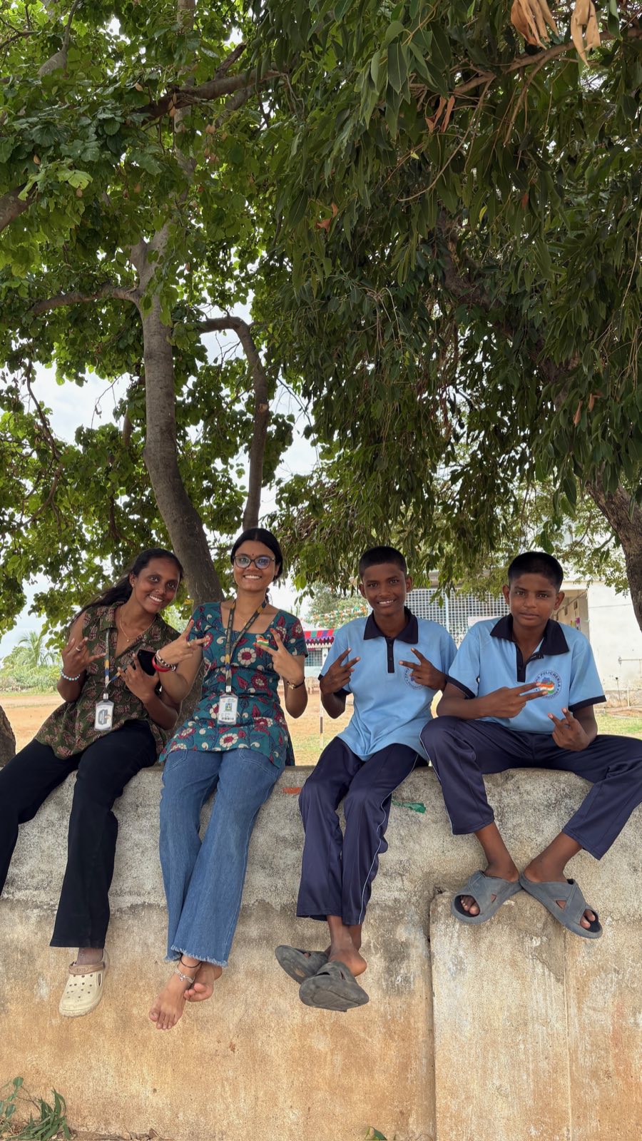 Two Street Cause VNR volunteers and two schoolboys sitting on a low wall under a tree, all making peace signs